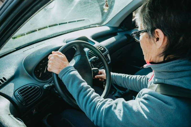 Oude bestuurder handen houden het stuur vast tijdens het rijden in een auto | auto rijden na herseninfarct | Rijbewijsdokter