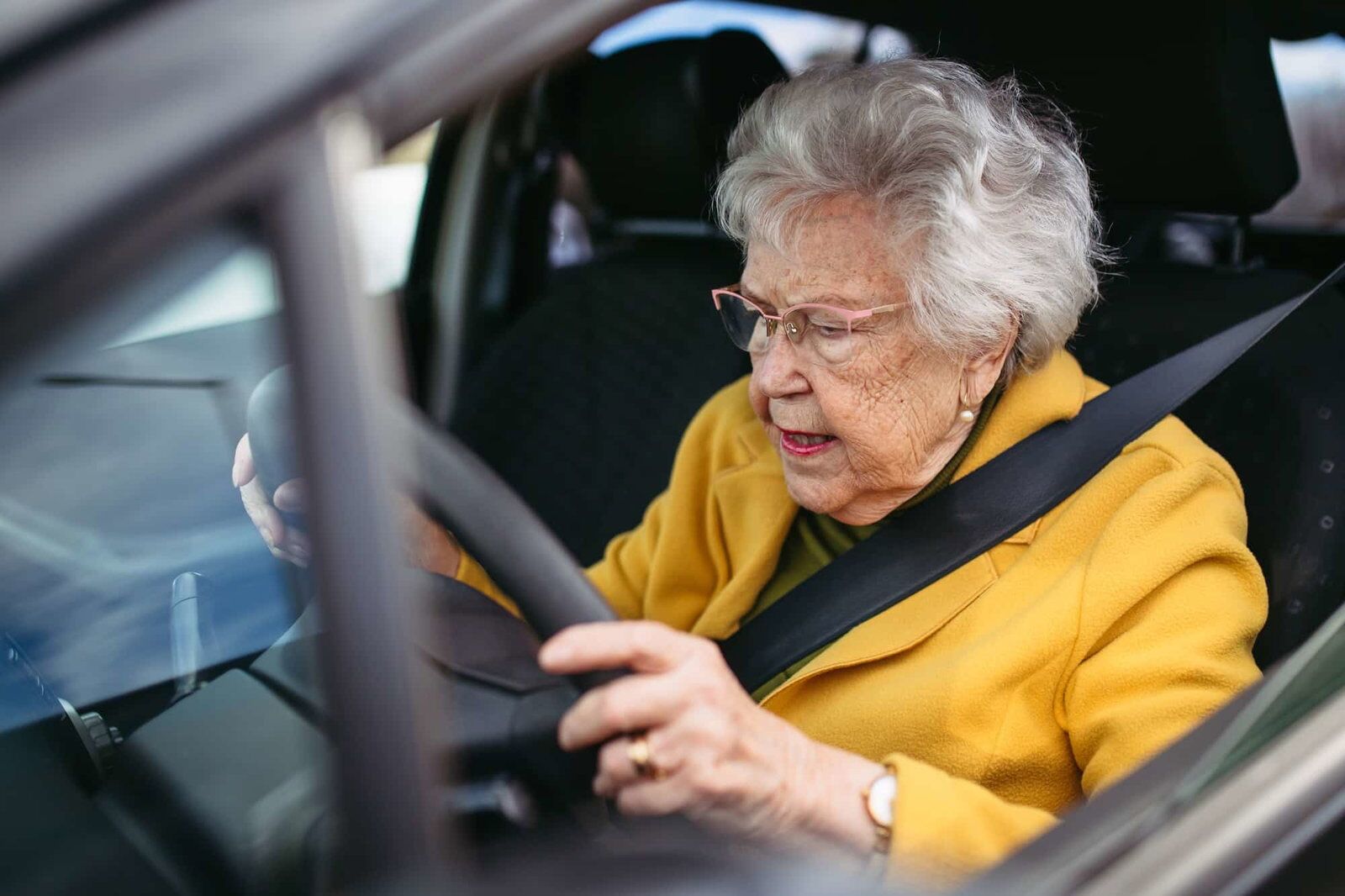 Geconcentreerde oudere vrouw rijdt alleen in de auto, houdt het stuur stevig vast. Veilig rijden voor ouderen | cbr dementie keuring | Rijbewijsdokter